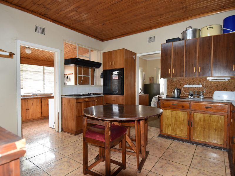 A dated kitchen featuring timber cabinetry, a wood-paneled ceiling, tiled flooring, and a convenient pass-through window connecting to the adjacent room.