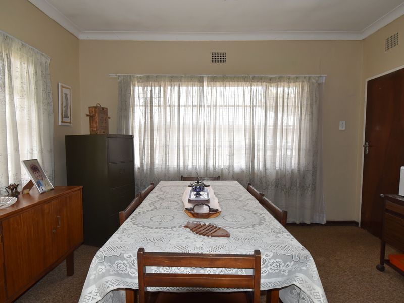 A functional dining room featuring carpeted flooring, neutral wall tones, and natural light through large windows.