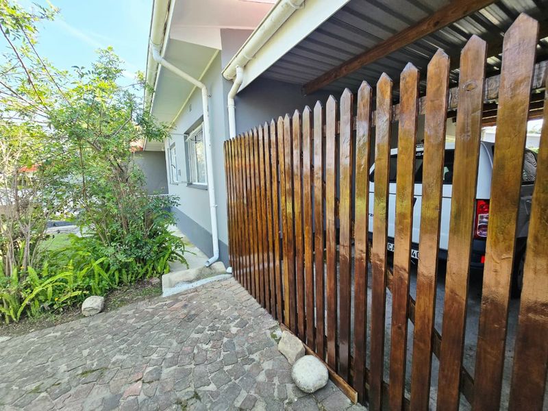 A view of the front exterior featuring a wooden picket fence, paved driveway, and a covered carport area.