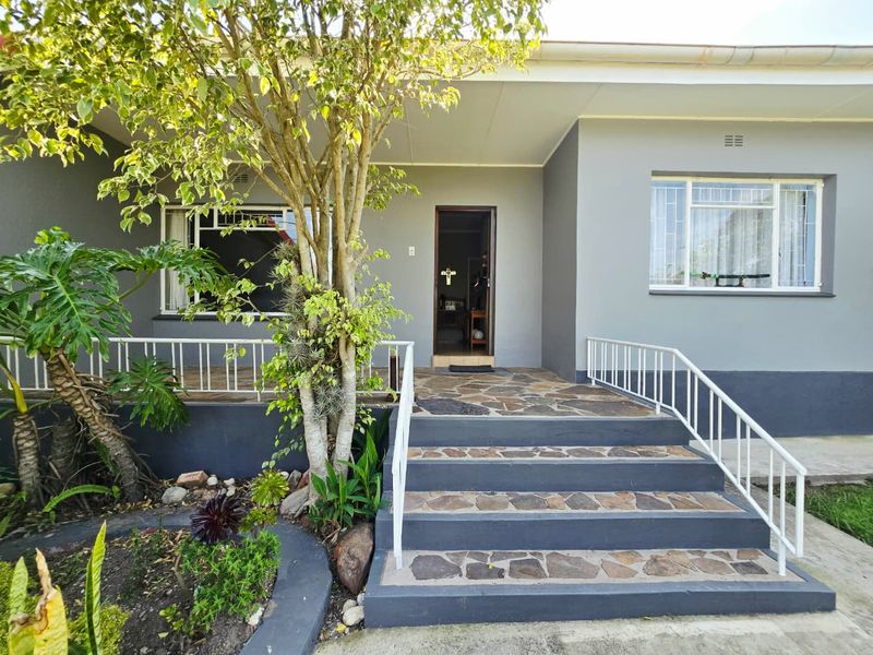 Front entrance of the house featuring stone-clad stairs, metal railings, and a covered porch area with security bars on the windows.
