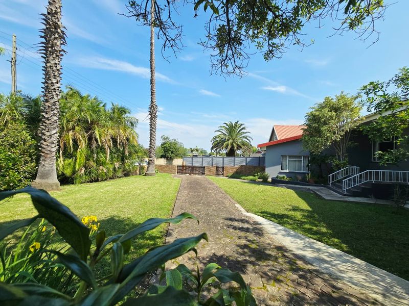 A well-maintained front garden featuring a cobblestone driveway, established palm trees, and a secure perimeter wall with gated access.