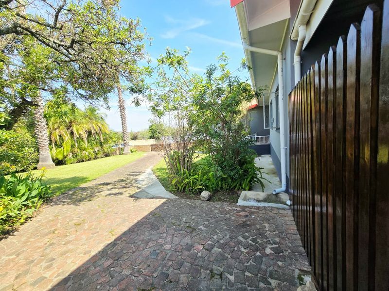 A view of the rear garden area featuring cobblestone paving, established landscaping, and a timber boundary fence along the side of the house.