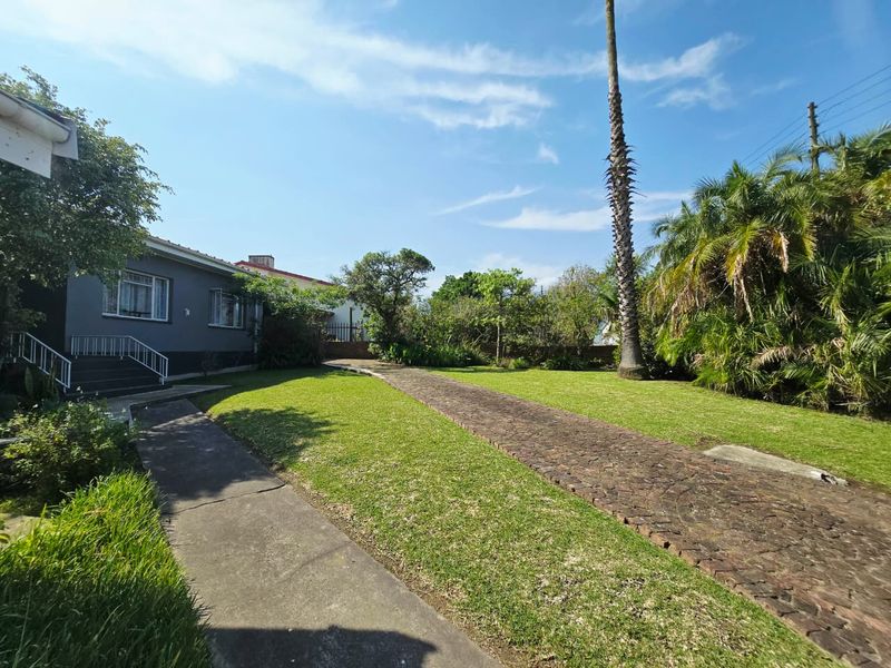 A view of the front exterior of the house featuring a well-maintained lawn, a paved driveway, and established garden landscaping.