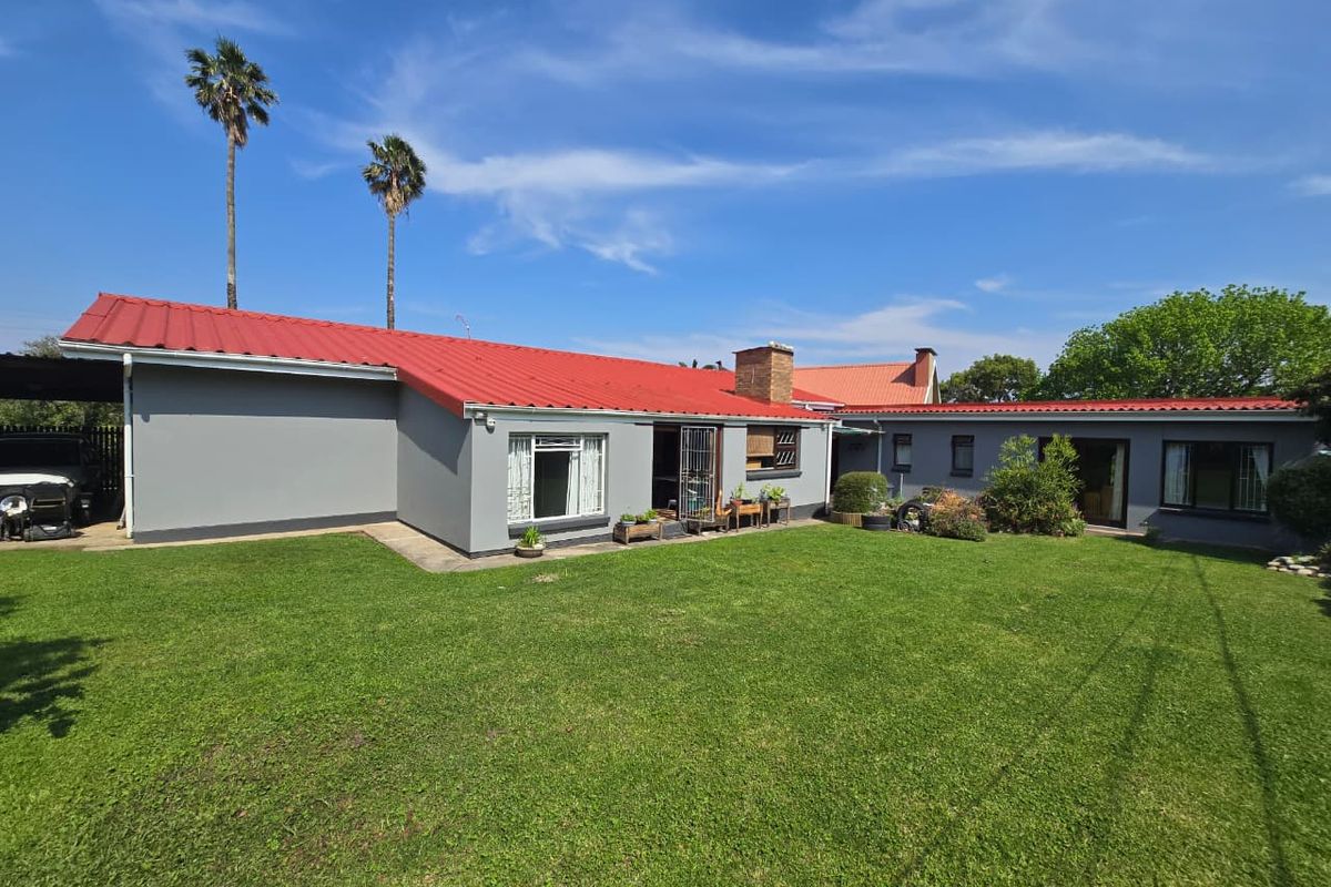 Rear view of the house featuring a red metal roof, brick chimney, and a spacious lawn area.