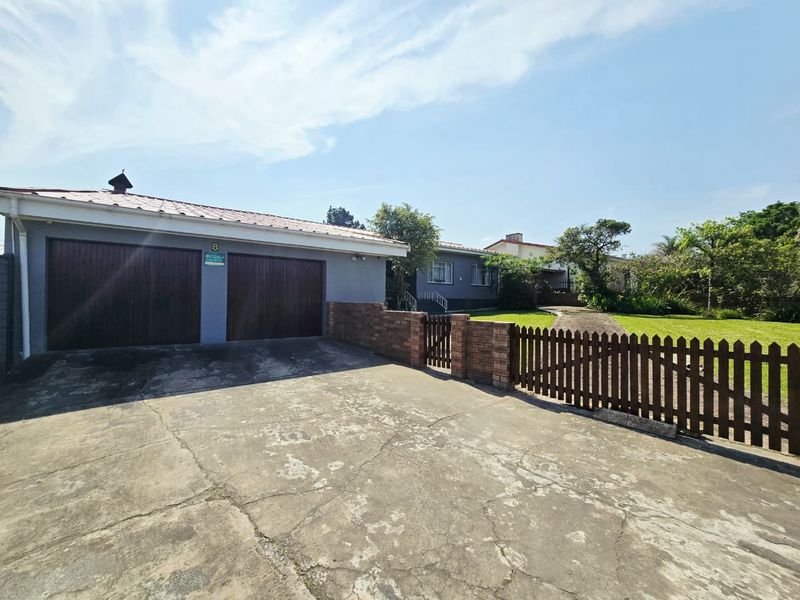 Front exterior view of the property featuring a double garage, concrete driveway, and a fenced garden area.
