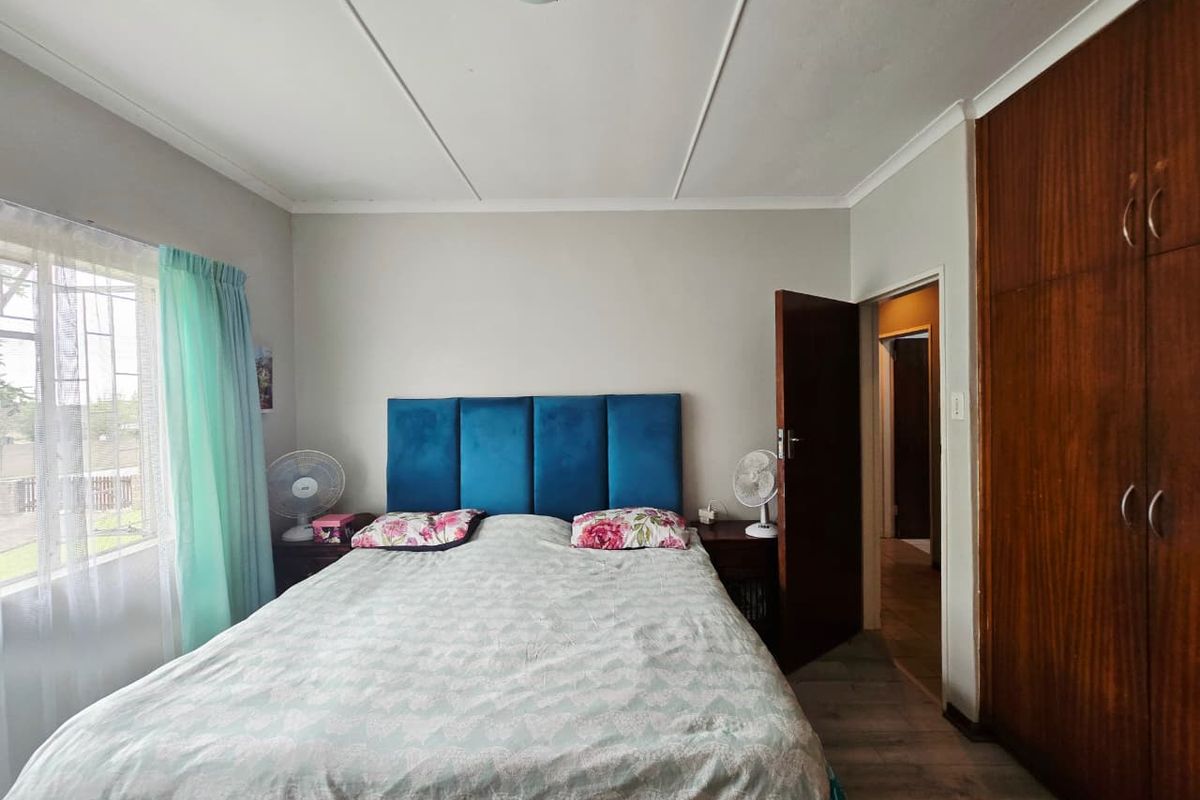 A functional bedroom featuring a built-in wooden wardrobe, neutral wall finishes, and a window with security bars.