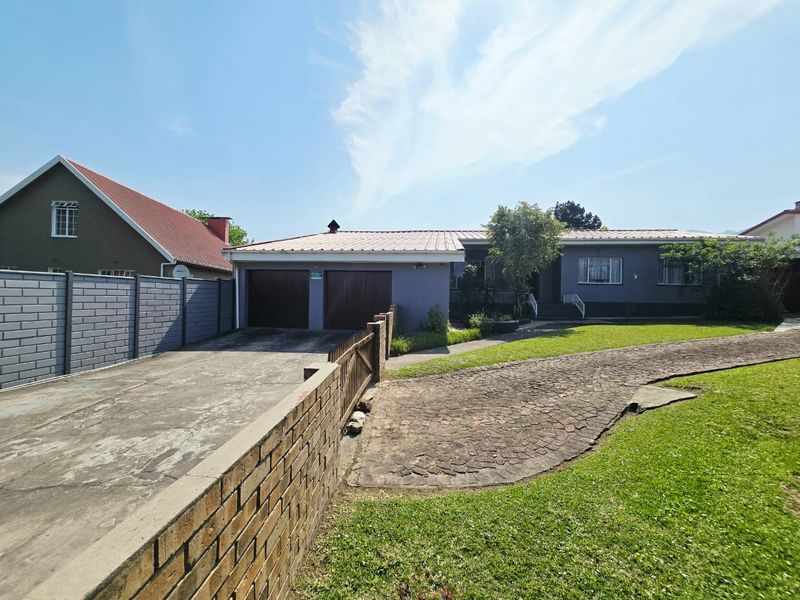 Front view of a residential property featuring a double garage, paved driveway, and a well-maintained lawn with brick boundary walling.