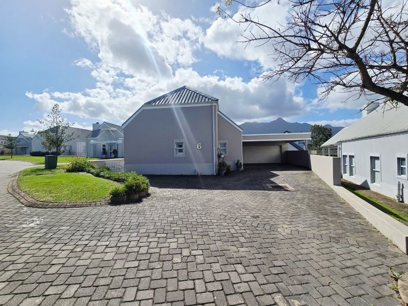 Front exterior view of the property featuring a paved driveway, attached carport, and well-maintained garden area with mountain views in the background.