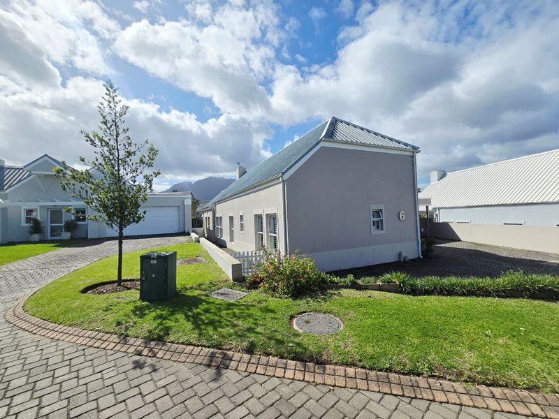 A well-maintained single-story residential property featuring a metal roof, paved driveway, and landscaped front garden area.