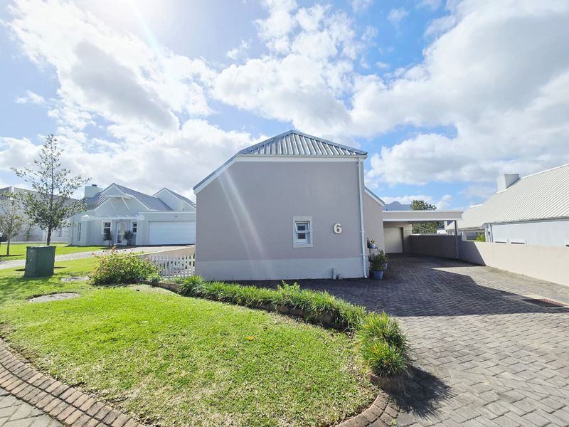 A well-maintained residential property featuring a paved driveway, carport, and neat front lawn with a picket fence.