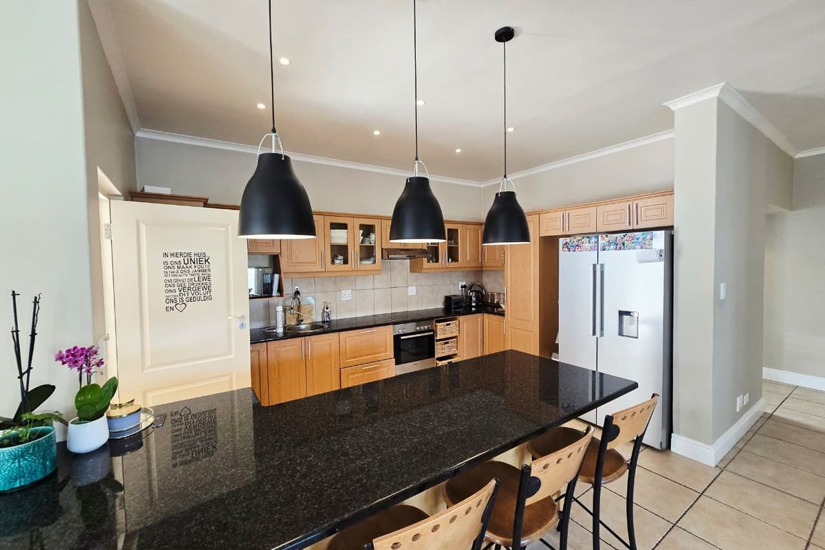 A functional kitchen featuring wooden cabinetry, granite countertops, a central island with breakfast bar seating, and integrated appliances.