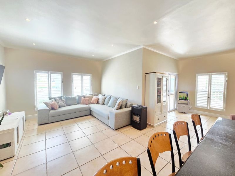 Spacious open-plan living area featuring neutral tiled flooring, recessed downlights, and plantation shutters, providing a bright and functional layout.
