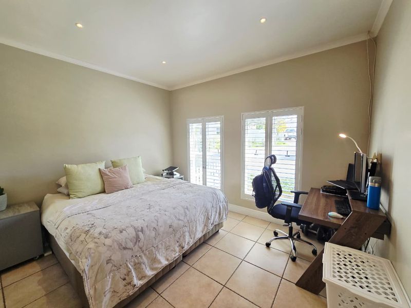 A well-lit bedroom featuring tiled flooring, recessed downlights, and double glass doors with white plantation shutters providing natural light.