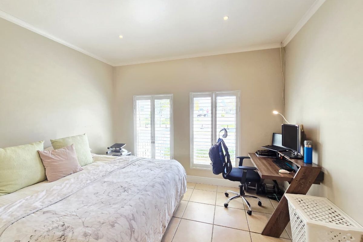 A well-lit bedroom featuring neutral walls, tiled flooring, and white plantation shutters, providing a functional space with natural light.