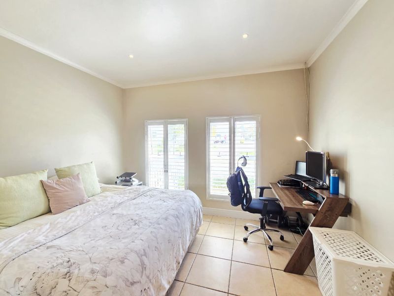 A well-lit bedroom featuring neutral walls, tiled flooring, and white plantation shutters, providing a functional space with natural light.