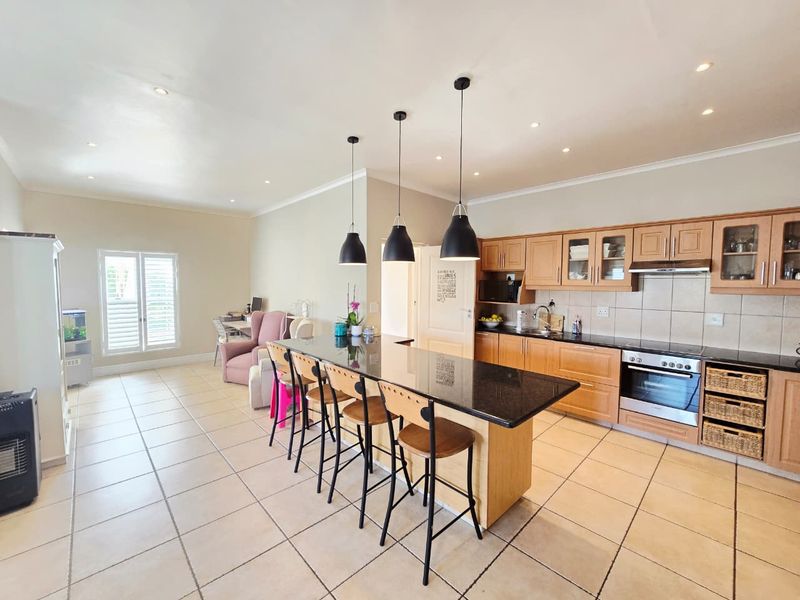 Spacious open-plan kitchen and living area featuring a large granite-topped island, built-in cabinetry, tiled floors, and modern recessed lighting.