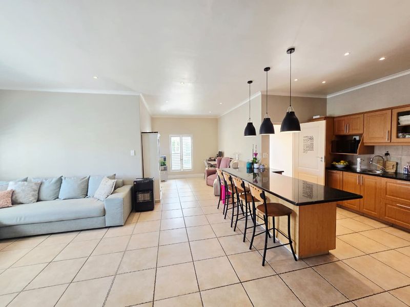Spacious open-plan living area featuring a kitchen with wooden cabinetry, granite island countertop, tiled flooring, and recessed lighting throughout.