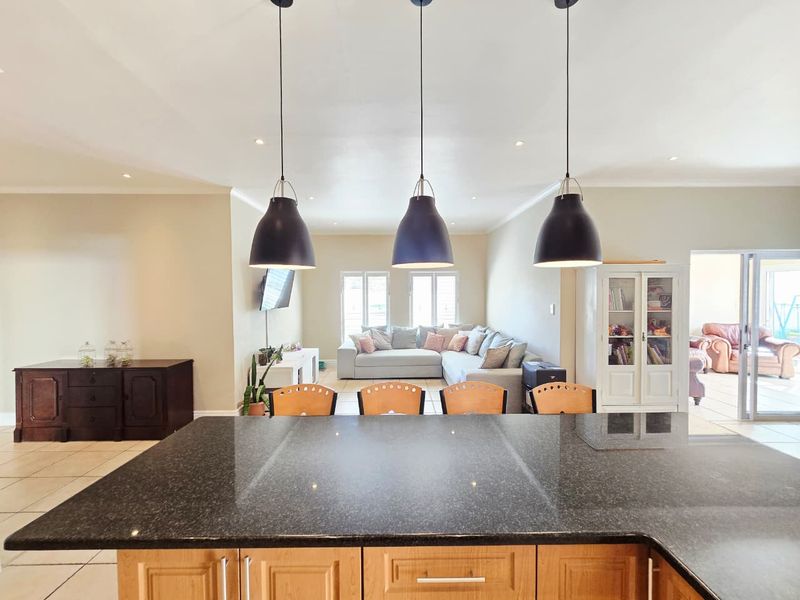 Spacious open-plan living area featuring a large kitchen island with granite countertops, pendant lighting, and seamless flow to the lounge and outdoor access.