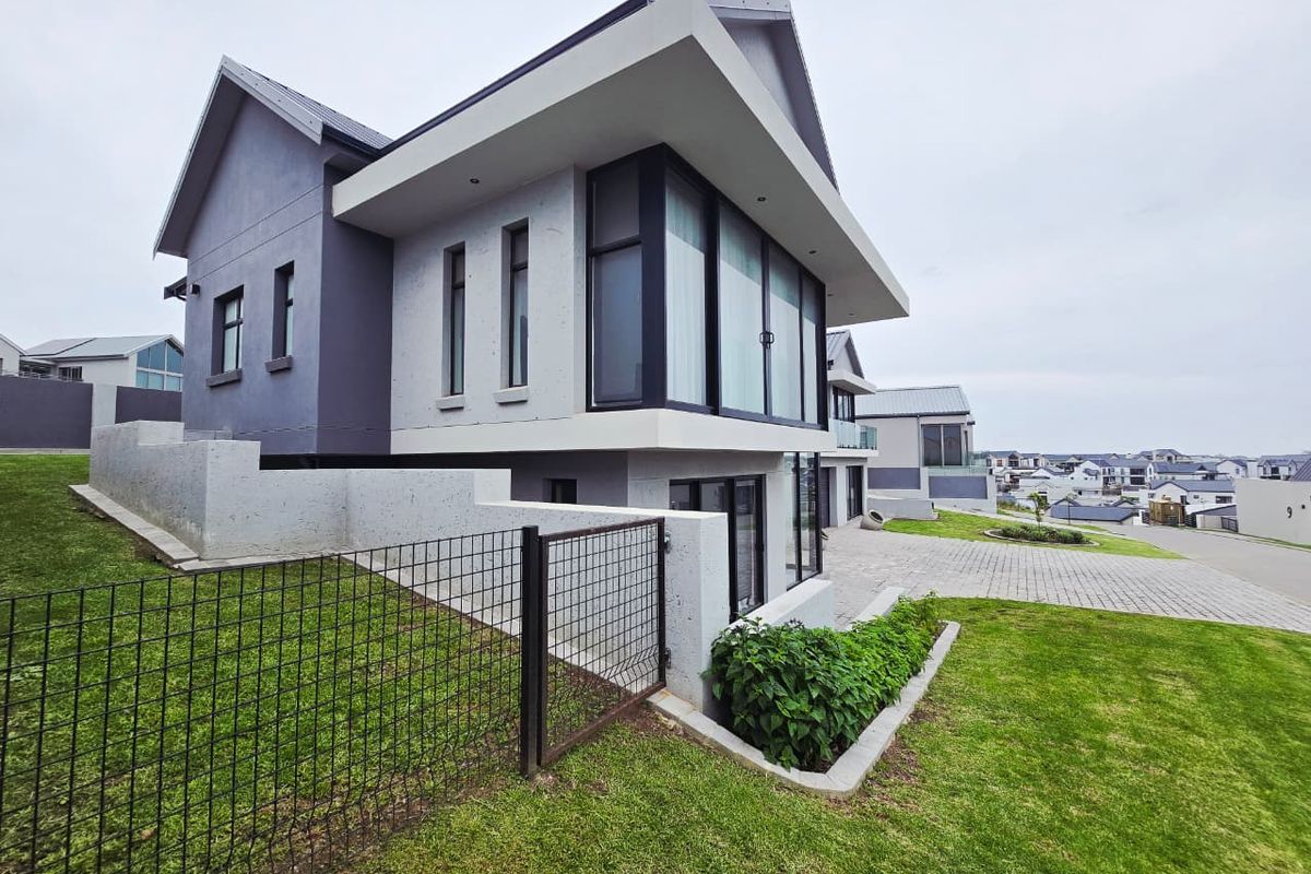 A modern double-story residential property featuring a paved driveway, landscaped lawn, and contemporary architectural design with large glass windows.