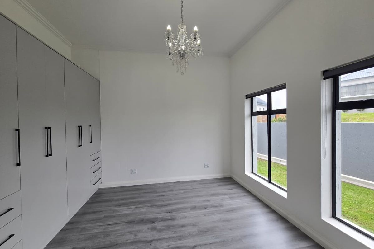 A bright, modern bedroom featuring sleek built-in cupboards, contemporary grey laminate flooring, and large windows overlooking the garden.