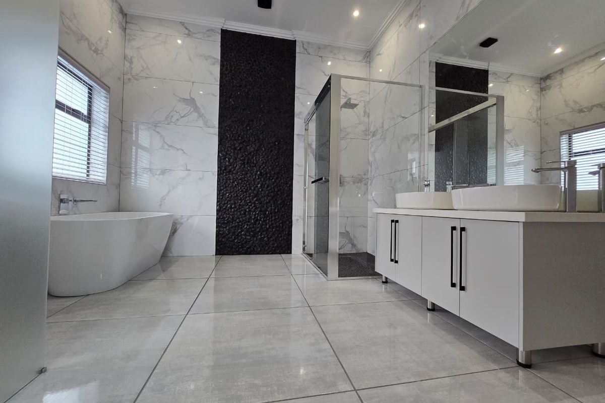 Modern, high-end bathroom featuring a freestanding bathtub, glass-enclosed shower, double vanity with contemporary fixtures, and elegant marble-look tiling.