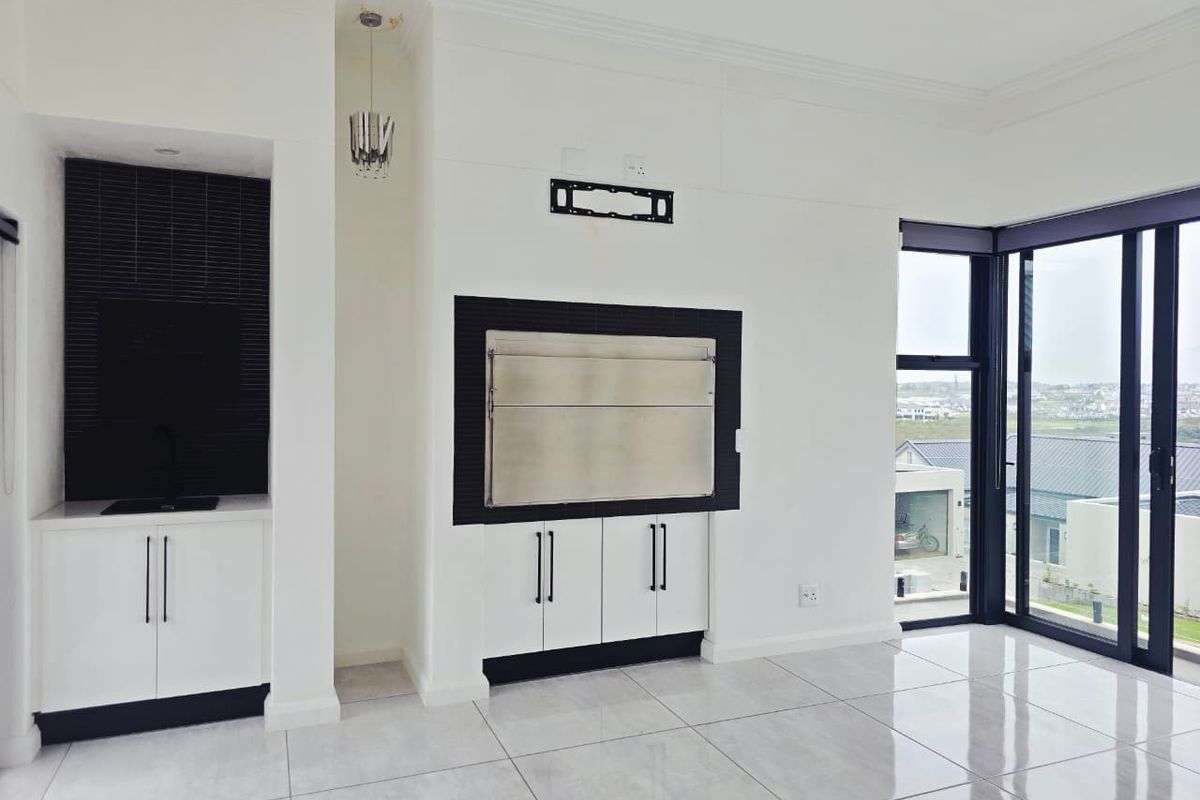 Modern living area featuring a built-in braai, sleek cabinetry with a sink, large aluminium sliding doors, and polished floor tiles.
