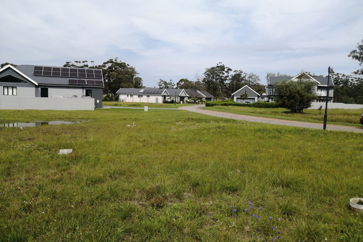 A view of a residential estate featuring multiple houses with solar panels, surrounded by open green space and a paved access road.