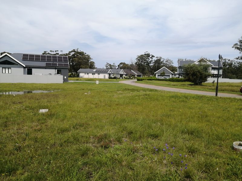 A view of a residential estate featuring multiple houses with solar panels, surrounded by open green space and a paved access road.
