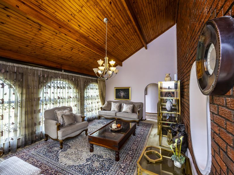 Spacious living room featuring a high raked timber ceiling, exposed brick wall, and arched windows, creating a warm and character-filled atmosphere.