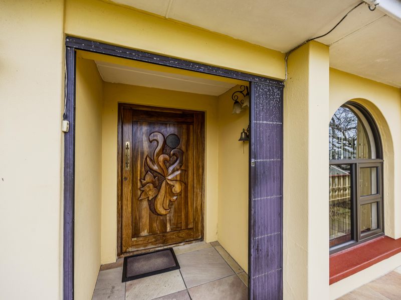 Covered front entrance featuring a decorative carved wooden door, arched window, and tiled porch area.