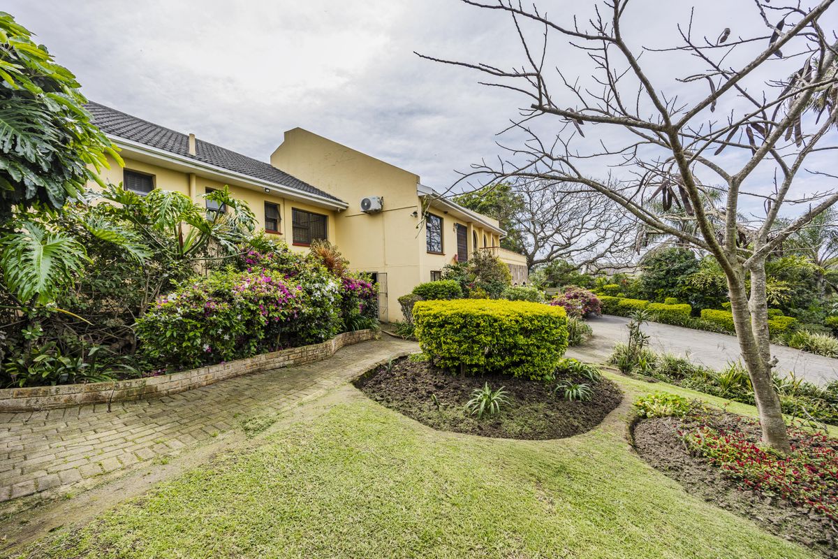 A view of the rear exterior of the house featuring a paved walkway, established garden beds, and a well-maintained lawn area.