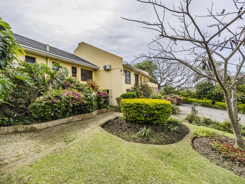 A view of the rear exterior of the house featuring a paved walkway, established garden beds, and a well-maintained lawn area.