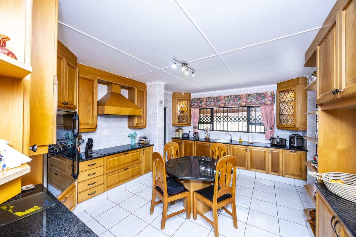 Spacious kitchen featuring extensive wooden cabinetry, granite countertops, built-in oven, extractor fan, and tiled flooring with a dedicated dining area.