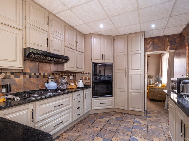 A functional kitchen featuring neutral-toned cabinetry, granite countertops, a gas hob with extractor fan, built-in oven, and durable tiled flooring.