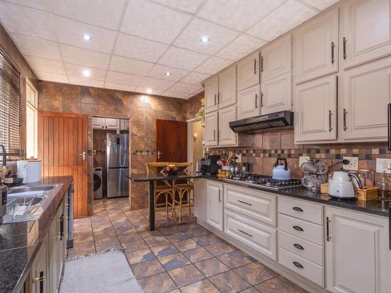 A functional kitchen featuring granite countertops, ample built-in cabinetry, a gas hob with extractor fan, and durable tiled finishes throughout.