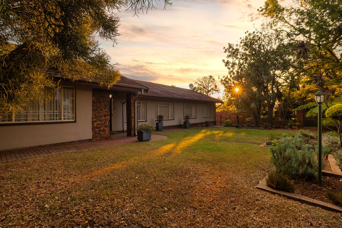 A well-maintained rear garden featuring a brick paved walkway, stone-clad facade details, and established landscaping at sunset.