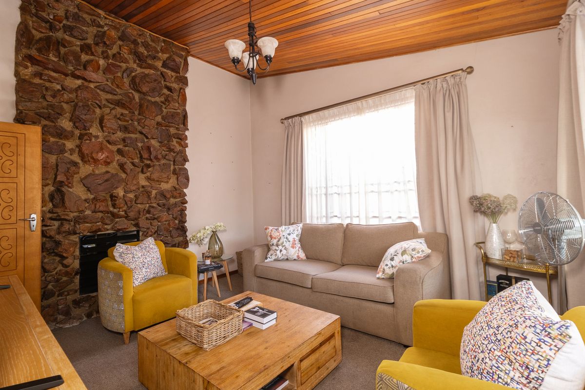 A cozy living room featuring a prominent stone fireplace, warm timber ceiling, and large window with curtains, creating a rustic and inviting atmosphere.