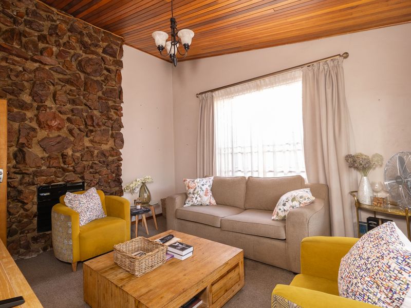 A cozy living room featuring a prominent stone fireplace, warm timber ceiling, and large window with curtains, creating a rustic and inviting atmosphere.