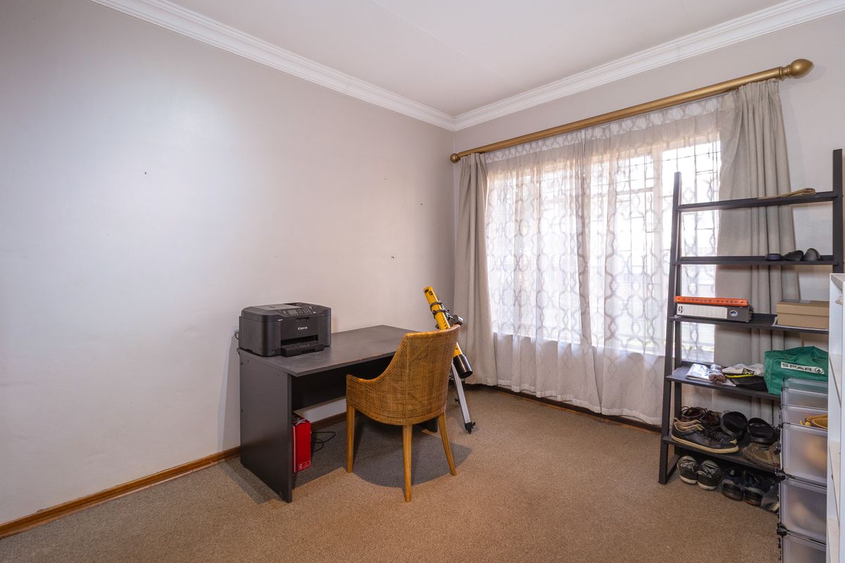 A functional bedroom featuring carpeted flooring, decorative cornice, and a large window fitted with security bars.