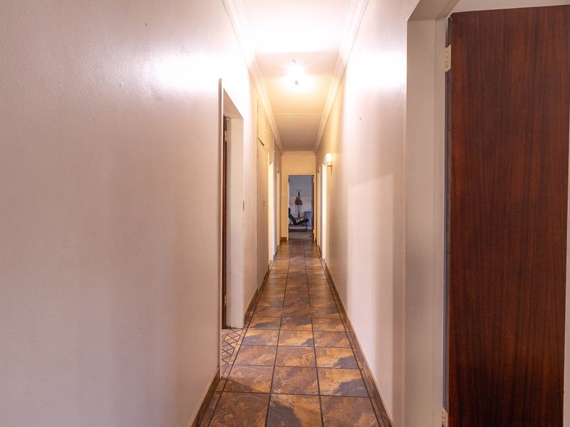 A long, empty residential hallway featuring tiled flooring and neutral walls, providing access to multiple rooms throughout the home.