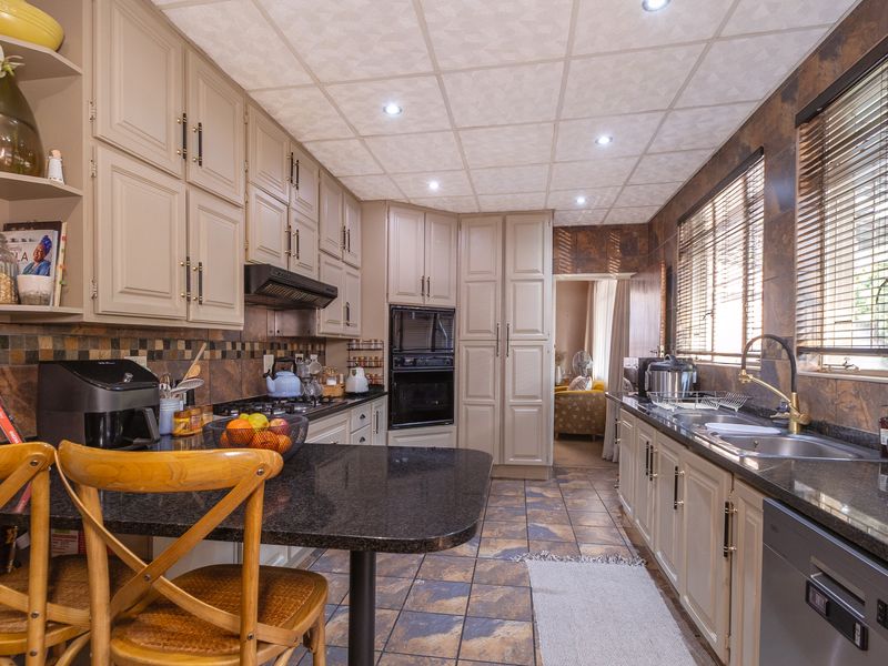 A well-maintained kitchen featuring granite countertops, built-in cabinetry, integrated appliances, and tiled finishes, offering a functional and classic cooking space.
