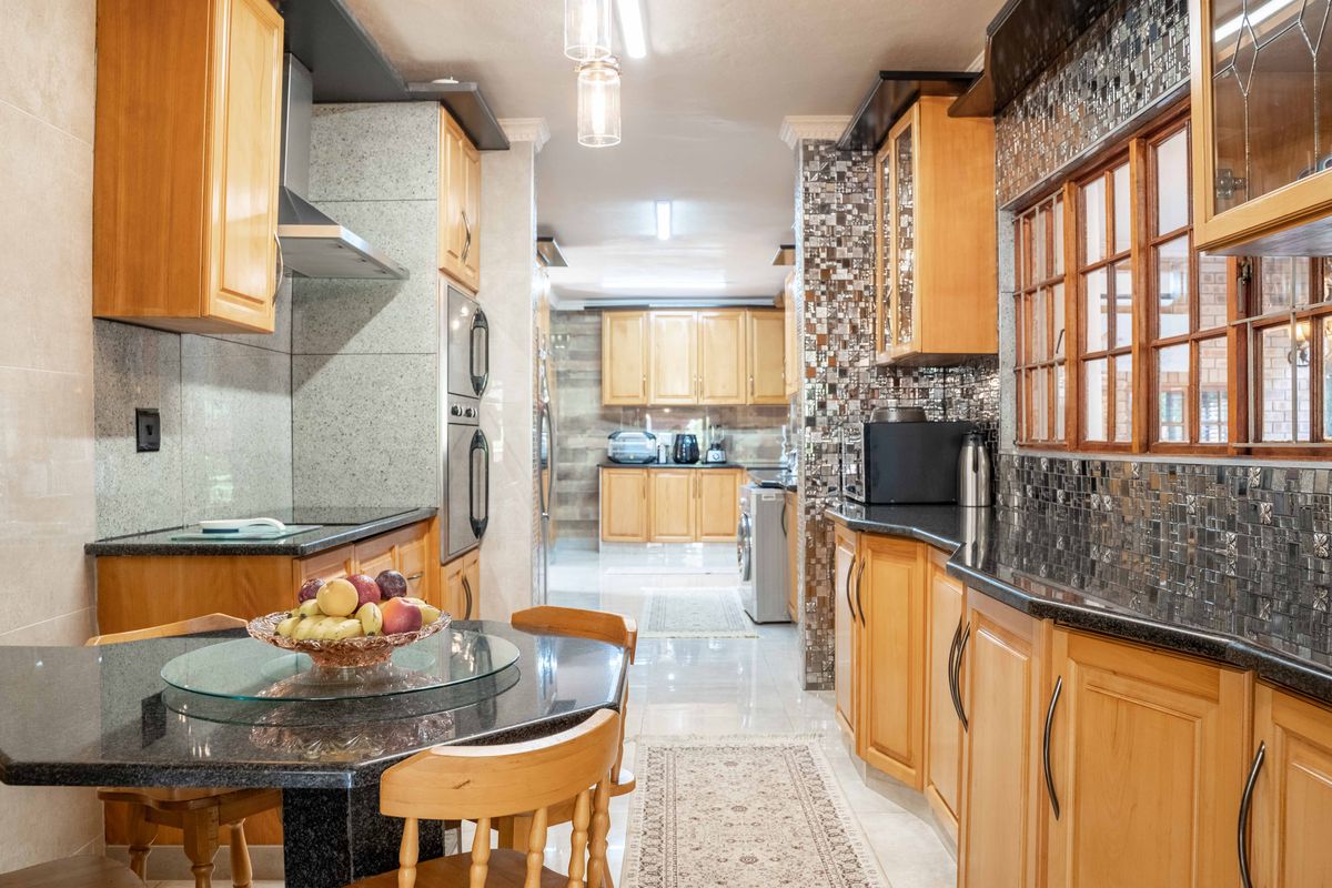 A spacious kitchen featuring extensive wooden cabinetry, granite countertops, mosaic tile backsplashes, and integrated appliances, offering a functional and well-maintained cooking environment.