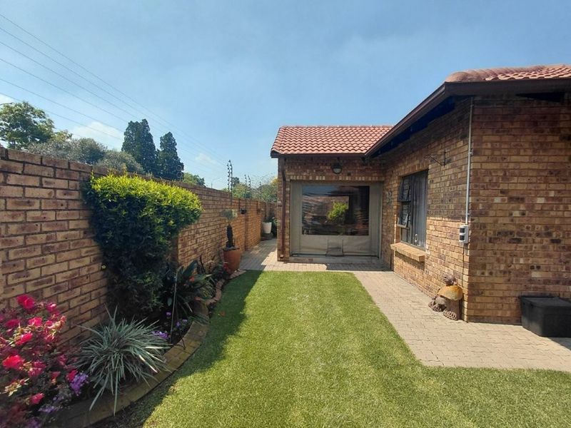 A well-maintained rear garden featuring a paved patio area, face brick exterior, and a lawn, enclosed by a perimeter brick wall with electric fencing.