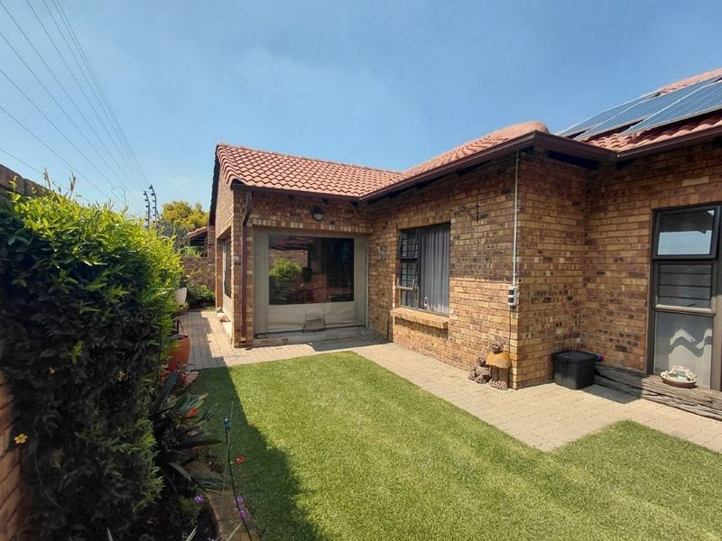 Rear view of the property featuring a face brick facade, tiled roof with solar panels, paved patio area, and a well-maintained lawn.
