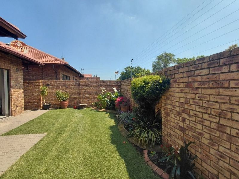 A private rear garden featuring a well-maintained lawn, paved patio area, and secure face brick boundary walls with electric fencing.