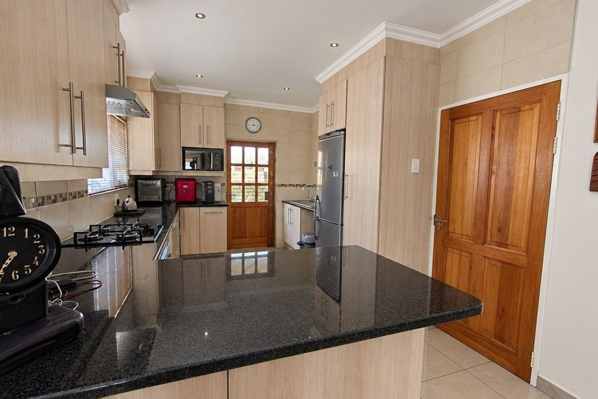 Modern kitchen featuring light wood cabinetry, dark granite countertops, gas hob, extractor fan, and tiled flooring with a solid timber door.