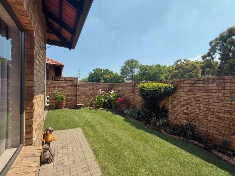 A well-maintained rear garden featuring a neat lawn, paved walkway, and secure face brick boundary walls with electric fencing.