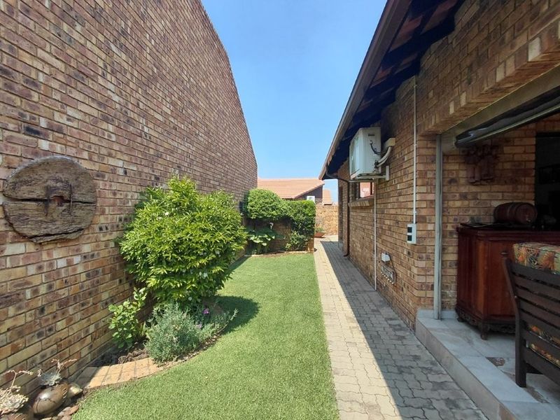 A side garden area featuring a paved walkway, well-maintained lawn, and face brick exterior walls with an integrated air conditioning unit.