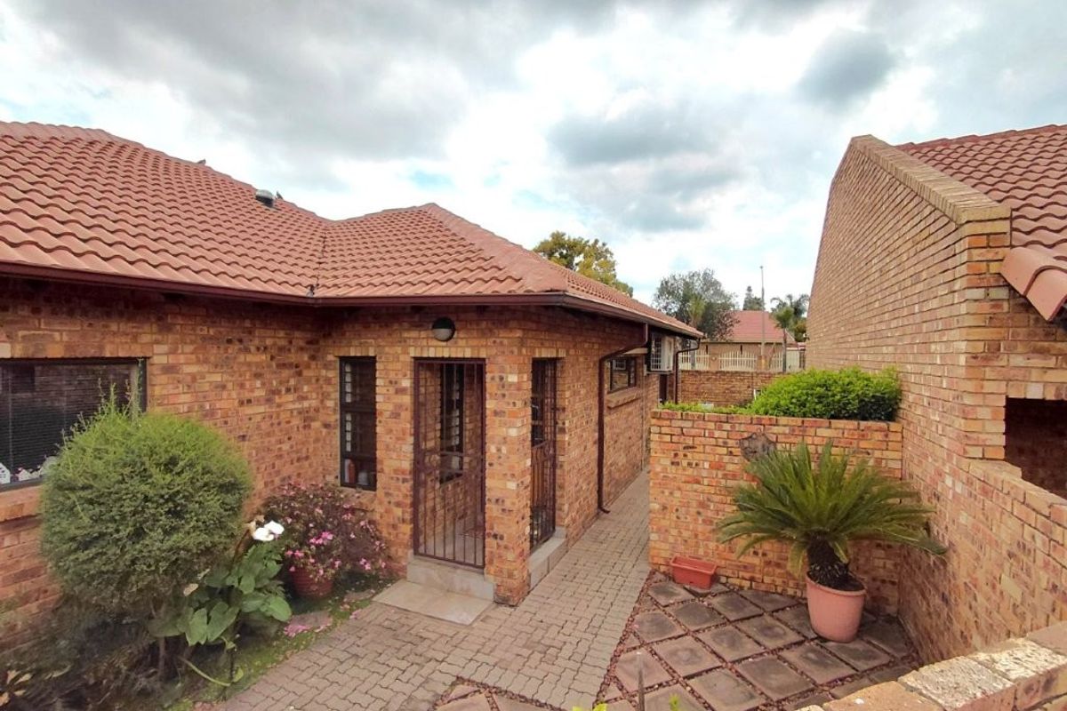 A well-maintained rear exterior view featuring face brick construction, a tiled roof, and a paved courtyard area with secure access.