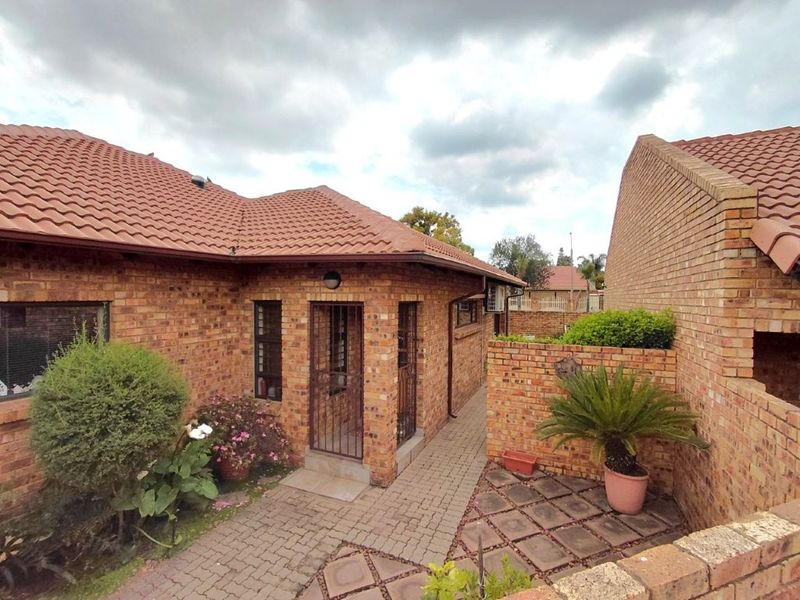 A well-maintained rear exterior view featuring face brick construction, a tiled roof, and a paved courtyard area with secure access.
